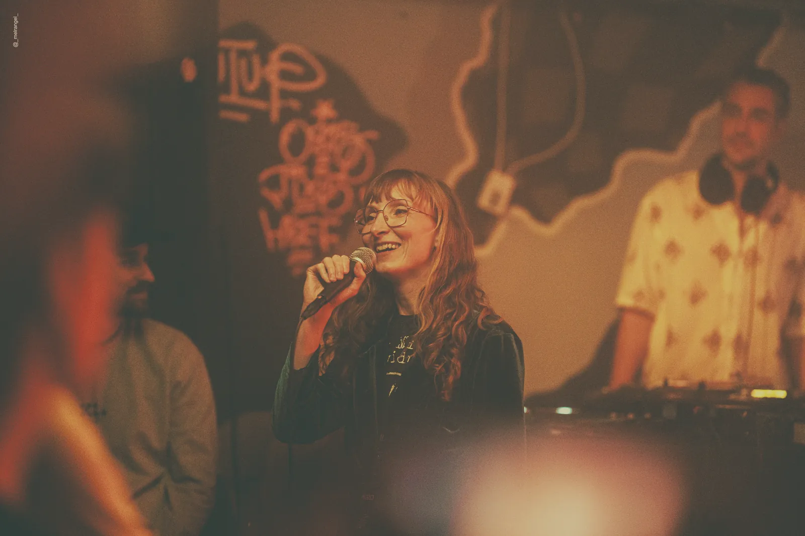 Sylvia singing in a dim club with a DJ behind her