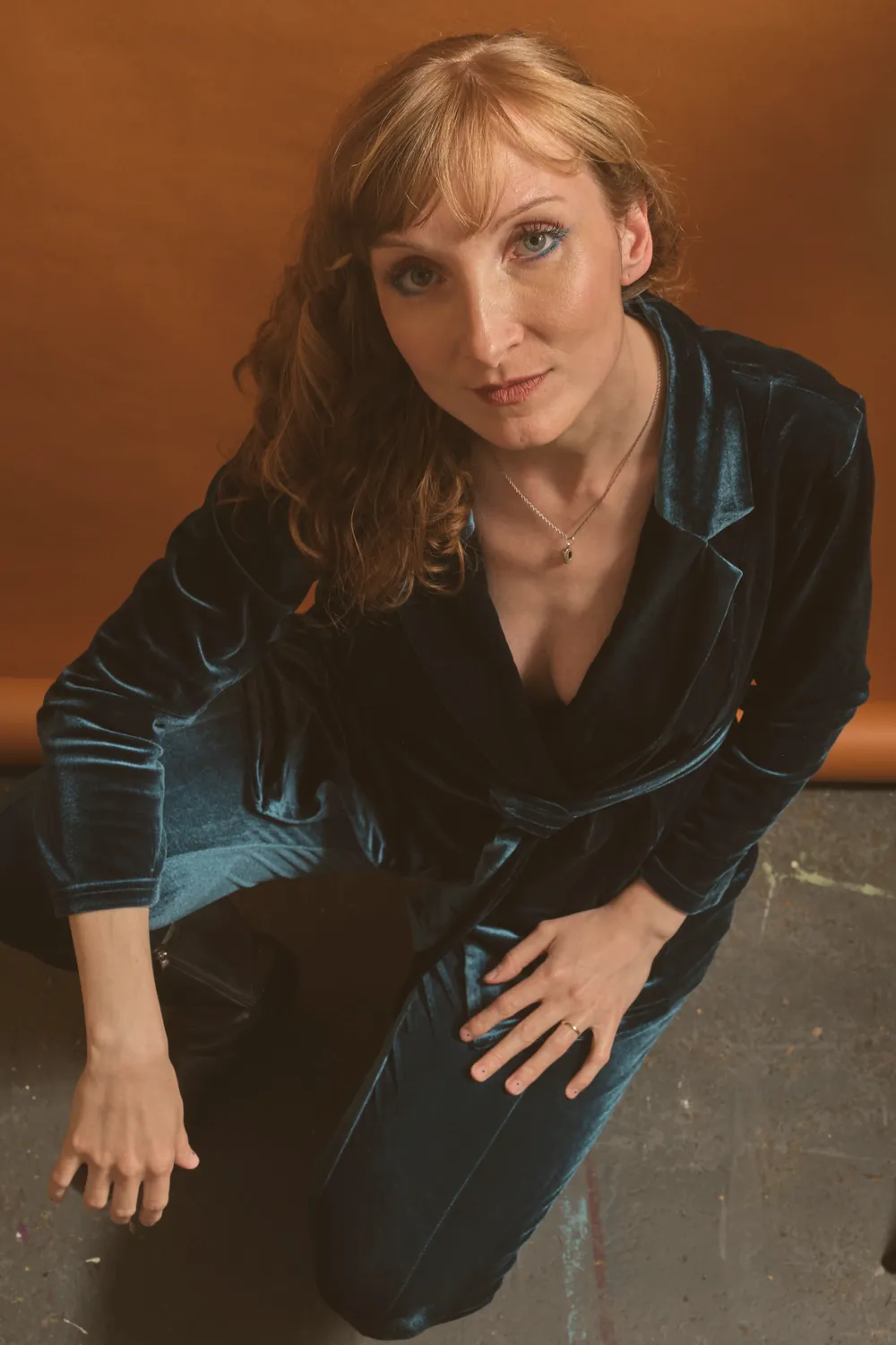 Sylvia Schmidt kneeling in a blue velvet suit against an ochre wall