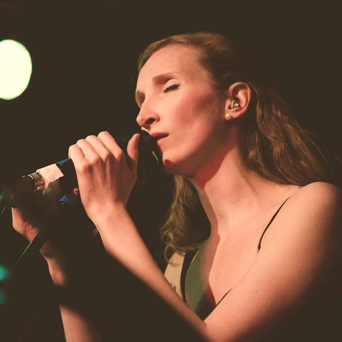 Sylvia singing with eyes closed, holding the microphone in both hands