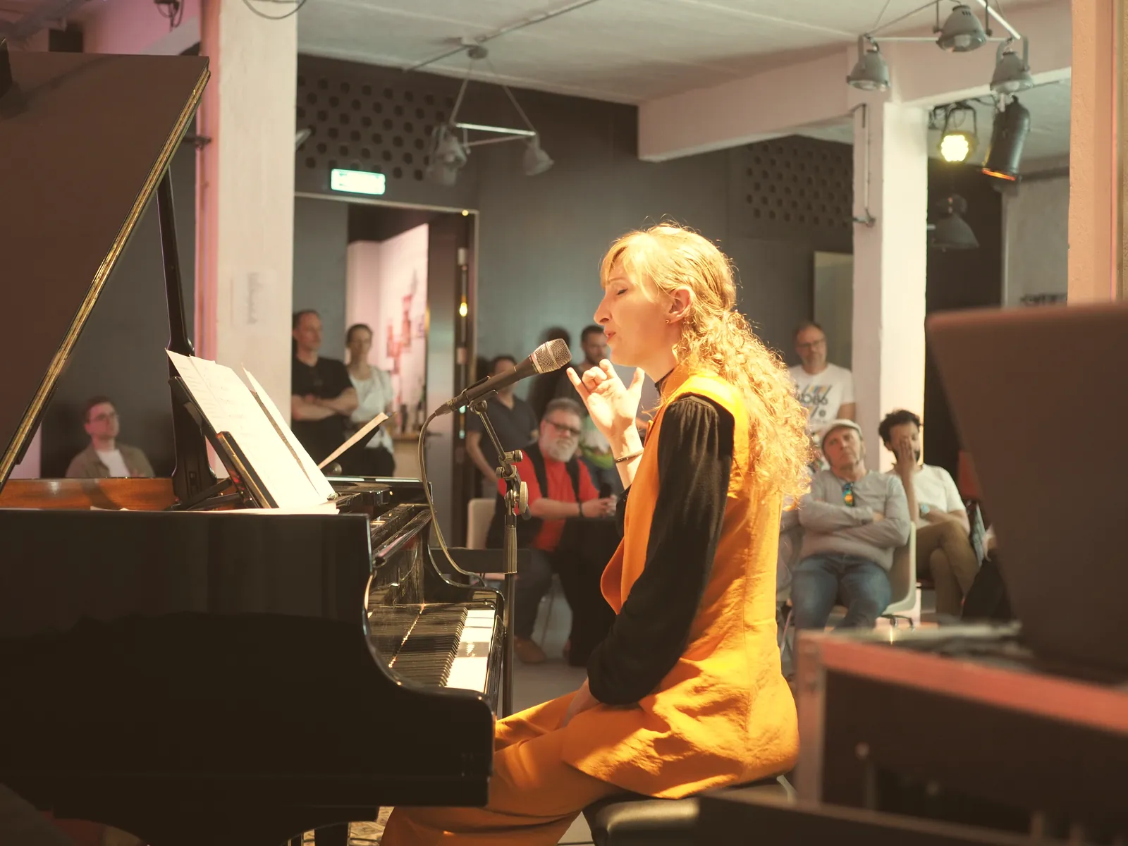 Sylvia singing at a grand piano in front of a seated audience