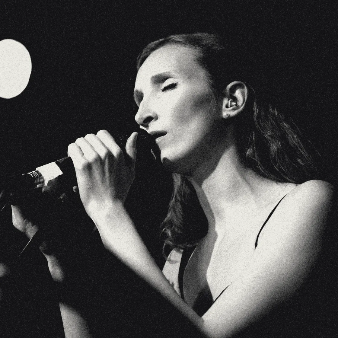 Sylvia singing with eyes closed, microphone in both hands