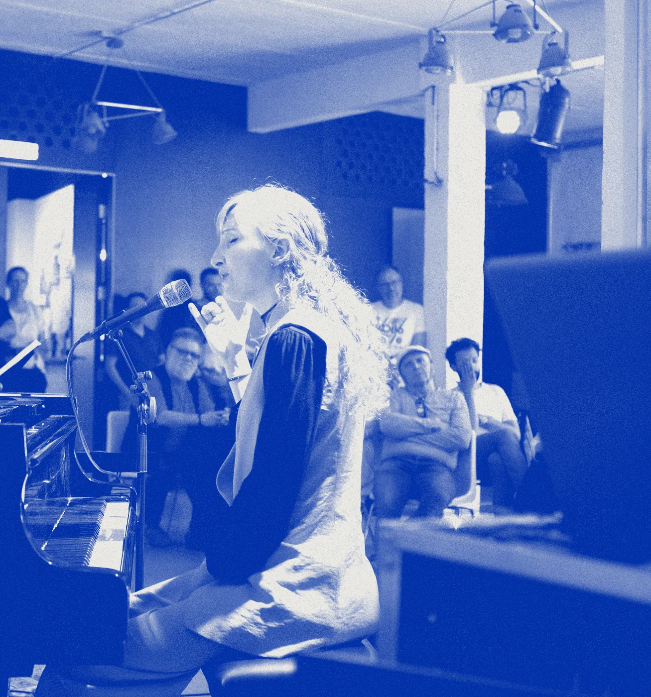 Sylvia singing at a grand piano before an audience, printed in blue